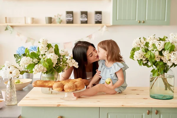 Mother\'s day greeting card. Family mother and baby daughter in morning have breakfast in kitchen. Spring card for Women\'s Day March 8. Happy family at home in kitchen. Family festive breakfast.