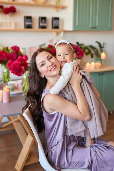 mom and daughter in elegant dresses in the kitchen, decorated with peonies