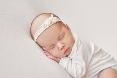 Yeni doğmuş tatlı bir kız bebek beyaz bir battaniyeye sarılmış yatıyor. Bebek eşyaları paketleme şablonu. Yüzünde gülümseme olan yeni doğmuş bir bebeğin yakın plan portresi. Sağlıklı ve tıbbi konsept. 