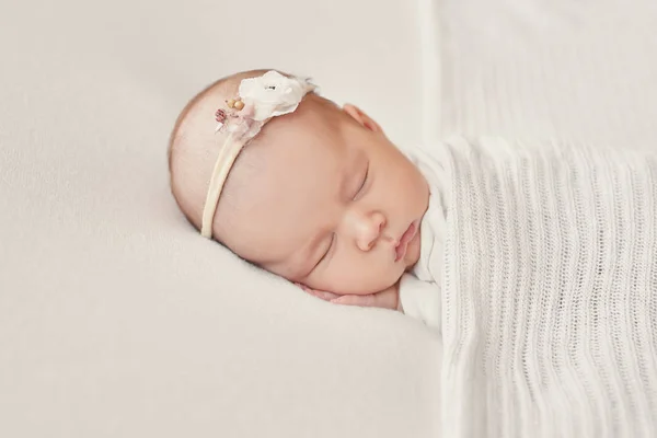 Yeni doğmuş tatlı bir kız bebek beyaz bir battaniyeye sarılmış yatıyor. Bebek eşyaları paketleme şablonu. Yüzünde gülümseme olan yeni doğmuş bir bebeğin yakın plan portresi. Sağlıklı ve tıbbi konsept. 
