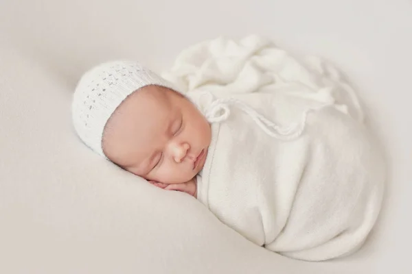 Yeni doğmuş şirin bebek beyaz bir battaniyeye sarılı yatıyor. Bebek eşyaları paketleme şablonu. Yüzünde gülümseme olan yeni doğmuş bir bebeğin yakın plan portresi. Sağlıklı ve tıbbi konsept. 