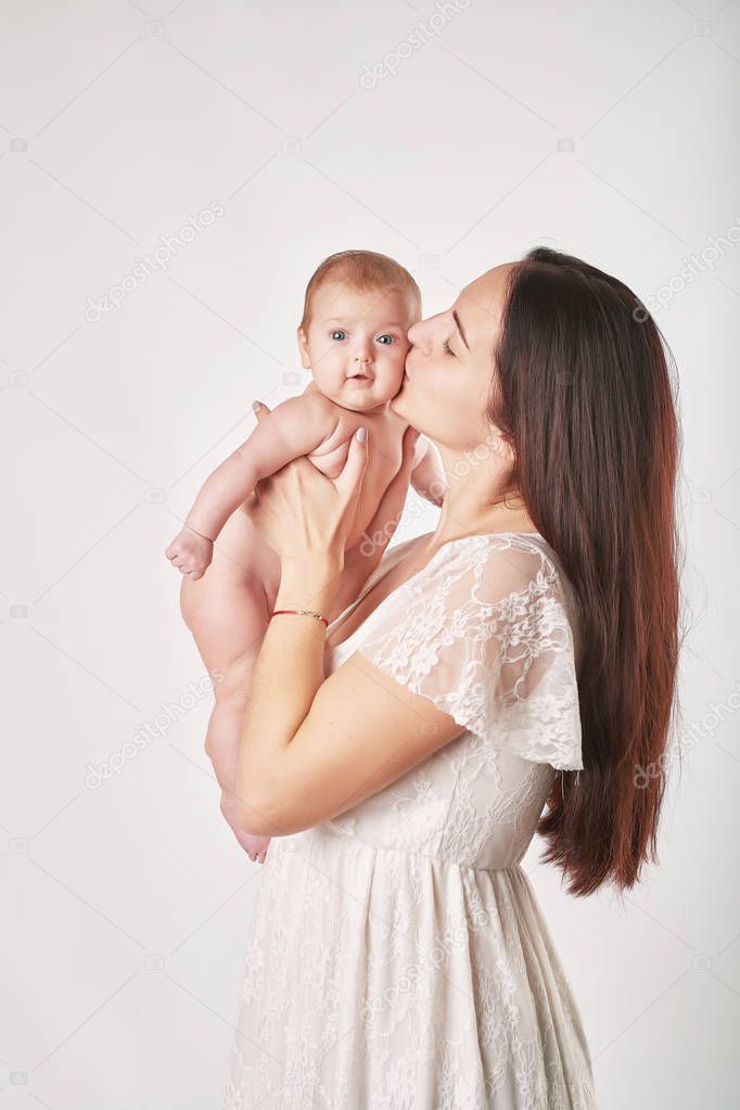 young mother with natural make-up holds the baby in her arms, shot on a light background