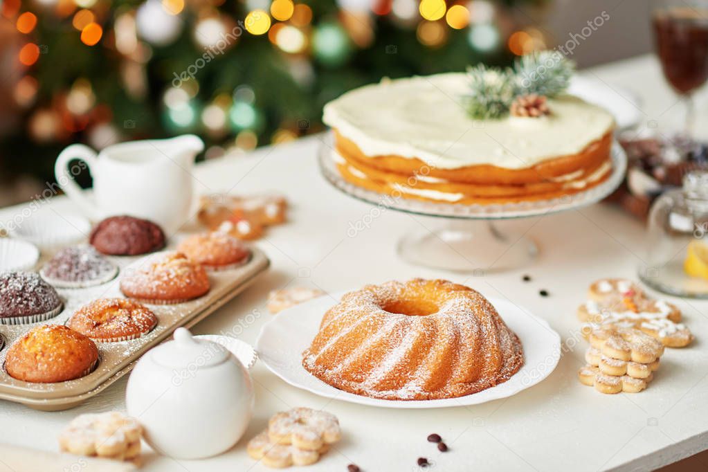 Christmas treats on the table: cupcake, naked cake, cookies and coffee with honey on the background of Christmas decorations