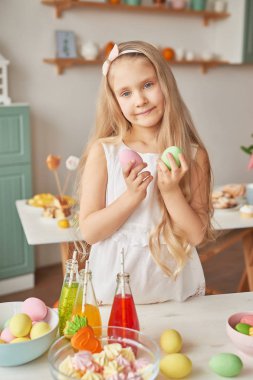 Girl in the kitchen on Easter day with Easter gingerbread and eggs