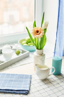 soyunma bir çay seti ve pencerenin karşısında masada bir vazoda gerbera