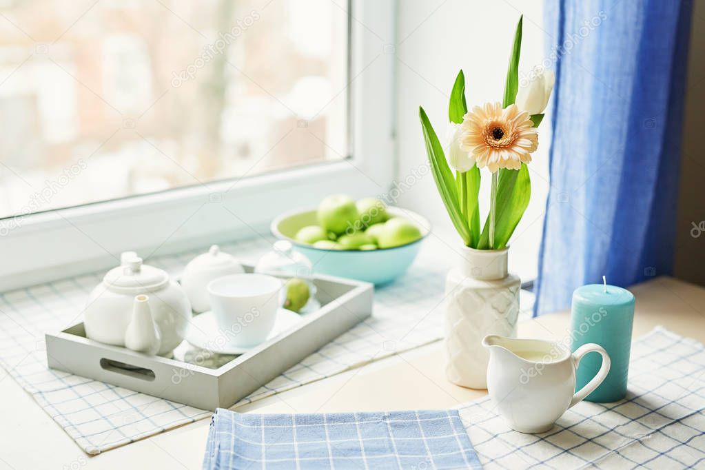 dressing with a tea set and a gerbera in a vase on the table opposite the window