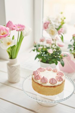 cama bir vazo bir tencerede gül ve lale ile yanındaki masada beze pasta