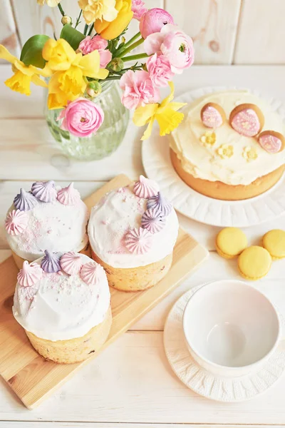 Easter cakes on the table, macaroons, eggs and a bouquet of flowers in a vase near on a white background