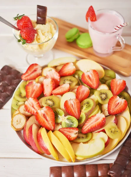 Chocolate bars and fruit sliced from strawberries, apples, bananas and kiwi on a wooden white background.