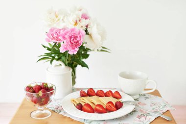 beyaz bir arka plan üzerinde şakayık ile bir vazo yakınında masada çilek ve kahve ile krep
