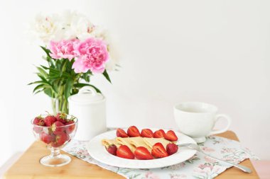 beyaz bir arka plan üzerinde şakayık ile bir vazo yakınında masada çilek ve kahve ile krep