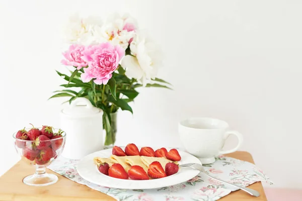 白い背景にピオニーと花瓶の近くのテーブルの上にイチゴとコーヒーとパンケーキ — ストック写真