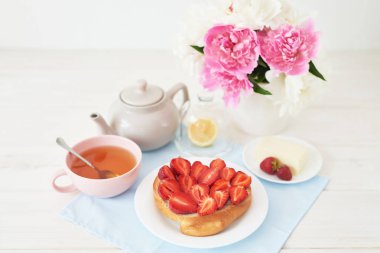 beyaz bir arka plan üzerinde şakayık ile bir vazo yakınında masada kruvasan ve çay ile çilek