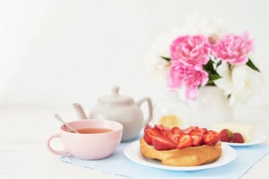 beyaz bir arka plan üzerinde şakayık ile bir vazo yakınında masada kruvasan ve çay ile çilek