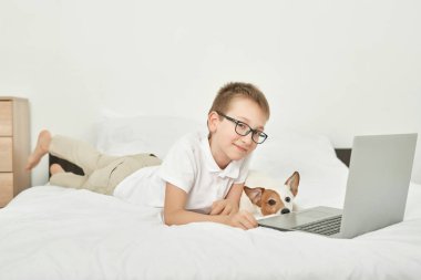 evde beyaz bir yatakta oturan köpek jack russell ile çocuk