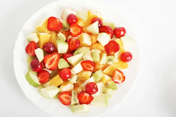 healthy food: fruit salad of oranges, strawberries, cherries, apples and kiwi in a plate on a white background, vegan and vegetarian food, ecological products