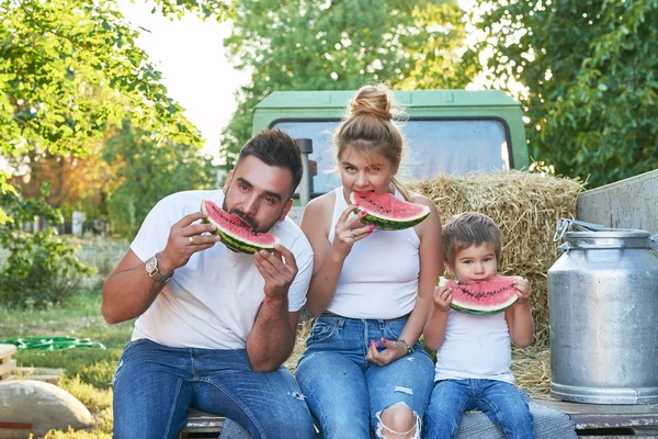 family with watermelons at the harvest next to a pickup truck in summer at sunset