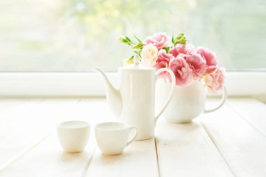 bir pencerenin arka planına karşı bir masa üzerinde çiçek bir vazo yanında kahve seti