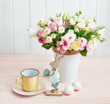 Mutlu Paskalya çiçekli tavşan tebrik kartı. Yumurtalı, tavşanlı ve çiçekli Paskalya masası. Beyaz arka planda bir buket gül ve mutluluk. Bahar konsepti Paskalya kahvaltısı. Kutlama tablosu dekoru.