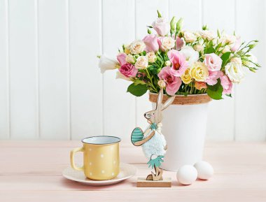 Mutlu Paskalya çiçekli tavşan tebrik kartı. Yumurtalı, tavşanlı ve çiçekli Paskalya masası. Beyaz arka planda bir buket gül ve mutluluk. Bahar konsepti Paskalya kahvaltısı. Kutlama tablosu dekoru.