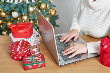Noel alışverişi. Kadın alıcı dizüstü bilgisayardan sipariş veriyor. Kadın hediyeler alır, Noel 'e hazırlanır, hediye kutuları ve paketlerin arasında. Kış tatili satışları. Mutlu Noeller ve mutlu yıllar..