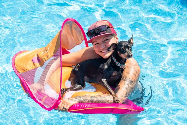 Woman relaxing with black pinscher dog on a flotation device in — Stock Photo, Image