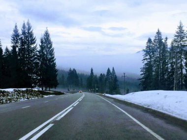 Bu resimde bir yoldan Romanya, kışın dağlardan sunulur, dağlar ve köknar ağaçları manzara sundu.