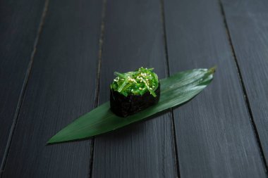 Japon Gunkan Maki suşisini Hiyashi wakame chuka ve bambu yaprağındaki susam tohumlarıyla kapatın. Görüntü mutfağı konsepti. Geleneksel Pan Asya restoran menüsü