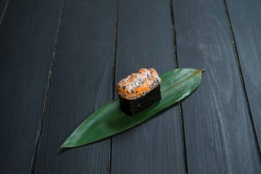 Japon Gunkan Maki Suşi 'sini somon ve bambu yaprağının üzerinde tobiko havyarı ile kapatın. Görüntü mutfağı konsepti. Geleneksel Sake maki suşi rulosu. Pan Asya restoran menüsü