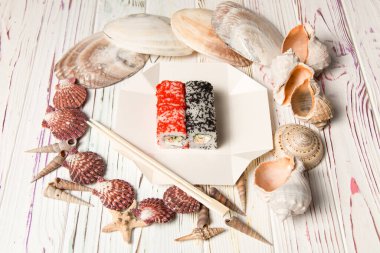 Japon suşi rulosu ve siyah ve kırmızı uçan balık yumurtası (Tobiko havyarı) yemek çubuklarıyla birlikte paket kutusunda. Kızarmış somon, salatalık, krem peynirli Asya yemeği. Tahtadaki deniz kabukları ve yıldızlar