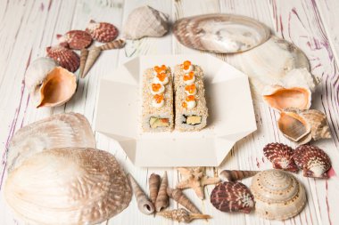 Asyalı Sushi 'nin ahşap arka planda, deniz kabukları ve yıldızlı paket servis kutusundaki yan görüntüsü. Somon, avokado, susam tohumu, Japon mayonezi ve kırmızı havyarla doldur..