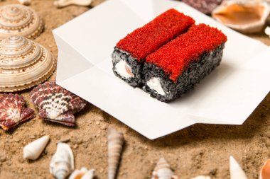 Japon suşi rulosu deniz kabukları ve yıldızlarla kumlu arka planda teslimat kutusunda. Somonlu siyah pirinç rulosu, Philadelphia krem peyniri ve uçan balık yumurtası (Tobiko havyarı). Asya menüsü deniz ürünleri yemeği