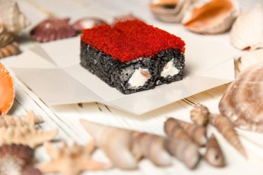 Japon suşi rulosu ahşap arka planda deniz kabukları ve yıldızlarla servis kutusunda. Somonlu siyah pirinç rulosu, Philadelphia krem peyniri ve uçan balık yumurtası (Tobiko havyarı). Asya menüsü deniz ürünleri yemeği