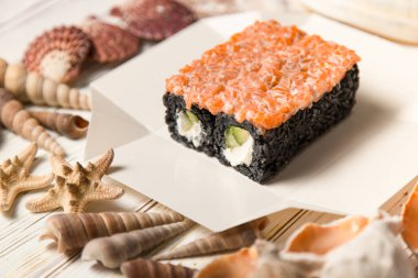 Japon suşi rulosu ahşap arka planda deniz kabukları ve yıldızlarla servis kutusunda. Avokado ve Philadelphia krem peynirli siyah pirinç rulosu. Asya menüsünde çiğ somon var.