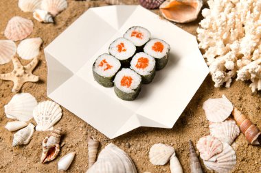 Japon Sake Maki Roll 'un yanına somon balığı ve beyaz karton kutunun üzerinde Norveç yosununa sarılmış pilav. Mercan, deniz kabukları ve kumsaldaki yıldızlar. Gıda dağıtım kreatice konsept menüsü