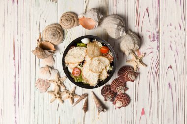 Sezar Salatası 'nın tavuklu fileto, vişneli domates, kızarmış ekmek, bıldırcın yumurtası ve siyah plastik kasede salata karışımı. Yemek paketi ve yemek. Tahta arka planda deniz kabukları ve yıldızlar