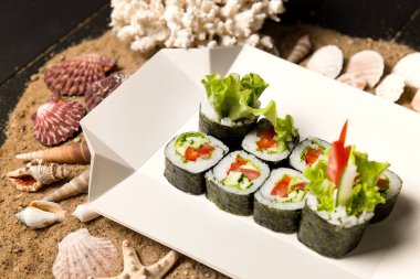 Japon Futomaki Sushi Roll parçaları karton teslimat kutusunda. Domates, salatalık, avokado, paprika, ahşap tahtada salata karışımı okyanus mercanı, deniz kabuğu ve kumdaki yıldızlar.