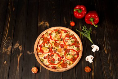 Biberli pizza, yeşil zeytin, füme sosis, mozzarella peyniri, pepperoni, salam, kırmızı biber, ahşap arka planda şampiyonlar. Malzeme ve bitkilerle lezzetli kesilmemiş pizza.