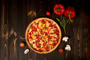 Biberli pizza, yeşil zeytin, füme sosis, mozzarella peyniri, pepperoni, salam, kırmızı biber, ahşap arka planda şampiyonlar. Malzeme ve bitkilerle lezzetli kesilmemiş pizza.