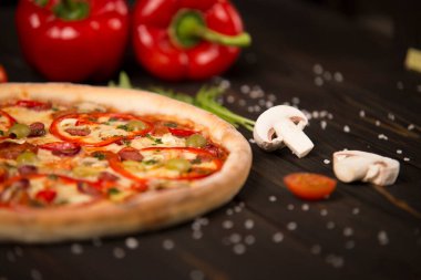 Biberli yarım pizza, yeşil zeytin, sosis, mozzarella peyniri, pepperoni, salam, kırmızı biber, ahşap tahtada iki dolmalık biber. Kesilmemiş pizzaya yaklaş
