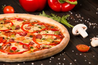 Biberli pizzanın bir kısmı, şampiyonlar, kiraz domatesleri, deniz tuzu ve ahşap arka planda otlar. Kesilmemiş pizzaya yaklaş
