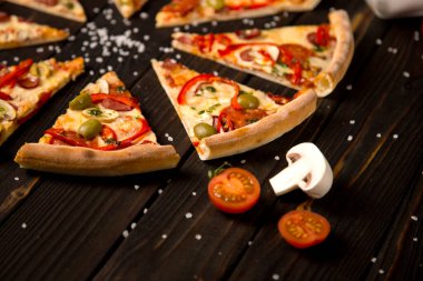 Dilimlenmiş pizzayı dolmalık biber, zeytin, sosis, mozzarella peyniri, pepperoni, salam, biber ve ahşap tahtada deniz tuzu, iki domates ve arka planda şampiyon ile kapatın. Kırsal yiyecekler