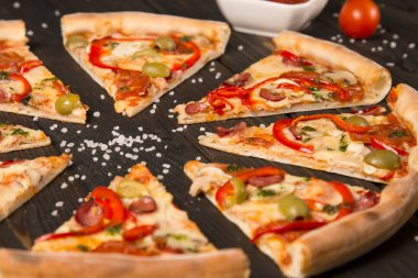 Lezzetli pizza dilimleri. Yanında dolmalık biber, zeytin, sosis, mozzarella peyniri, pepperoni, salam, acı biber, ahşap zemin üzerinde şampiyonlar ve odakta deniz tuzu..