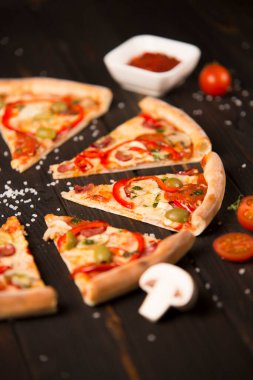 Biberli dilimlenmiş pizza, yeşil zeytin, sosis, mozzarella peyniri, pepperoni, salam, kırmızı biber, ahşap arka planda şampiyonlar. Lezzetli pizza parçaları. Fast food lezzetli yemekler.