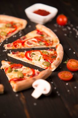 Dilimlenmiş pizzanın yarısı dolma biber, zeytin, sosis, mozzarella peyniri, pepperoni, salam, acı biber, ahşap tahtada şampiyonlar ve arka planda deniz tuzu ve malzemeler var..