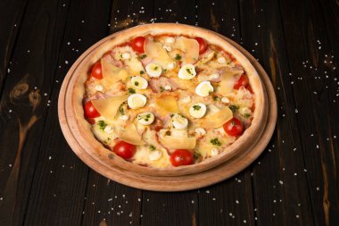 Kiraz domatesli pizza, pesto sosu, parmesan peyniri, tavuk filetosu, domuz pastırması, bıldırcın yumurtası ahşap zeminde mozzarella peyniri ve deniz tuzu. Tahtada dilimlenmemiş lezzetli pizza.