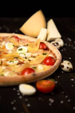 Kiraz domatesli İtalyan pizzası, pesto sosu, parmesan peyniri, peynir, tavuk filetosu, domuz pastırması, bıldırcın yumurtası, ahşap zemin üzerinde mozzarella peyniri deniz tuzu ve malzemelerle birlikte. Kesilmemiş pizzaya yaklaş