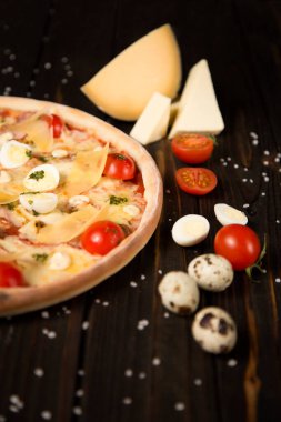 Kiraz domatesli pizzanın yarısı, pesto sosu, parmesan peyniri, peynir, tavuk filetosu, domuz pastırması, bıldırcın yumurtası, ahşap zemin üzerinde mozzarella peyniri deniz tuzu ve malzemelerle birlikte. Lezzetli kesilmemiş pizza.