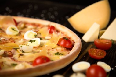 Kiraz domatesli İtalyan pizzası, pesto sosu, parmesan peyniri, peynir, tavuk filetosu, domuz pastırması, bıldırcın yumurtası, ahşap zemin üzerinde mozzarella peyniri deniz tuzu ve malzemelerle birlikte. Kesilmemiş pizzaya yaklaş