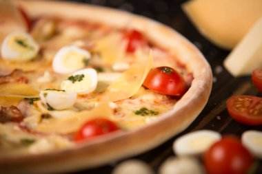 Çeri domatesli pizza, pesto sosu, parmesan peyniri, tavuk filetosu, domuz pastırması, bıldırcın yumurtası, ahşap zemin üzerinde mozzarella peyniri ve deniz tuzu ve malzeme. Kesilmemiş pizzanın yarısı.